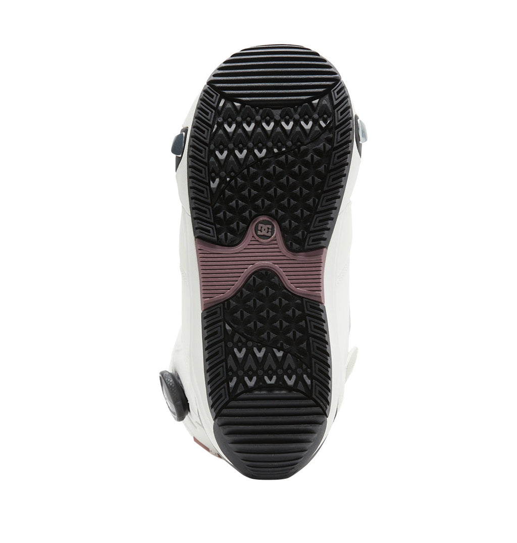 The image displays the bottom view of the DC Shoes Women’s Lotus Step On® Snowboard Boots in white, highlighting a black and brown textured rubber sole with geometric tread patterns for enhanced grip. These Step On boots are engineered to deliver optimal traction and stability on snowy terrain.