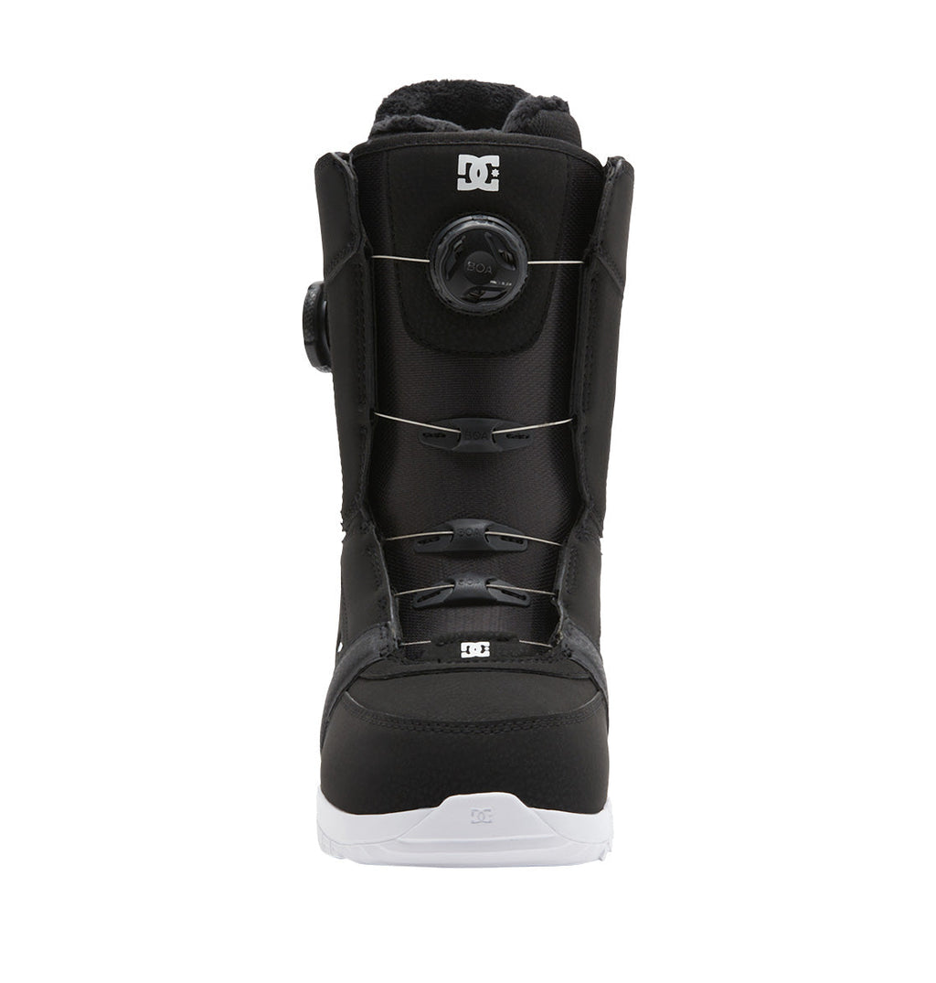 The DC Shoes Women’s Lotus BOA® Snowboard Boot is pictured centered and facing forward, showcasing its black design with a white Unilite outsole, a round BOA® Fit System tightening dial, and DC logo accents on the tongue and toe, photographed on a plain white background.