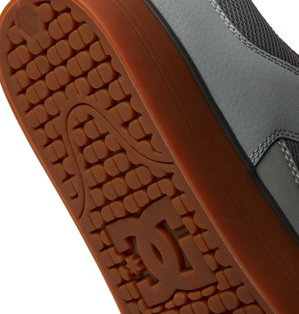 Close-up of the sole on the Men’s Pure Shoes by DC Shoes, showcasing a textured rubber tread with a stylized DC logo and curved line design. The shoe’s gray upper features visible stitching, combining versatile style with comfortable wear.