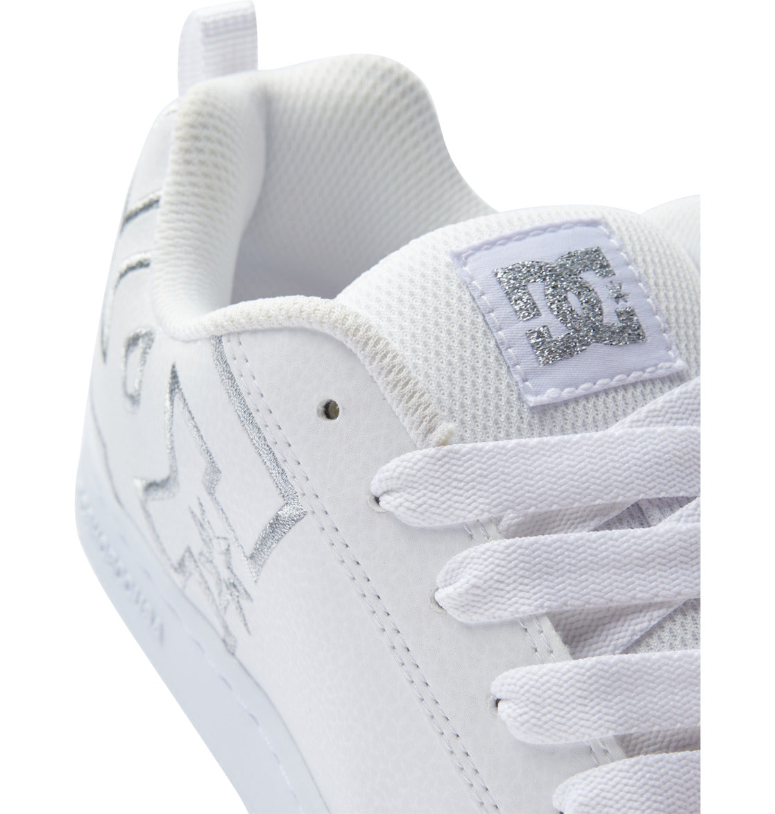 Close-up of the DC Shoes Women’s Court Graffik Shoes—a white chunky sneaker with white laces, silver stitching, and a textured white tongue adorned with a silver embroidered DC logo—an iconic nod to ‘90s style women’s sneakers.