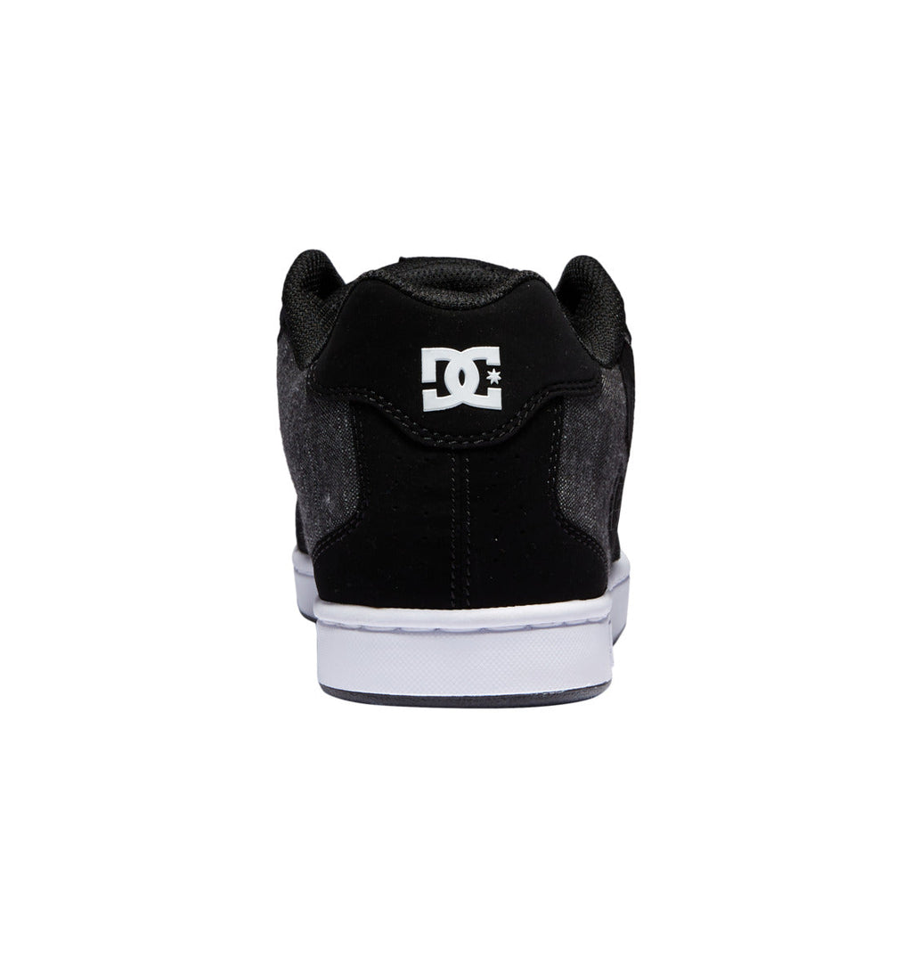 A rear view of the DC Shoes Men’s Net Shoes in black is displayed, featuring a white sole and the DC Shoes logo in white on the heel, set against a plain white background.