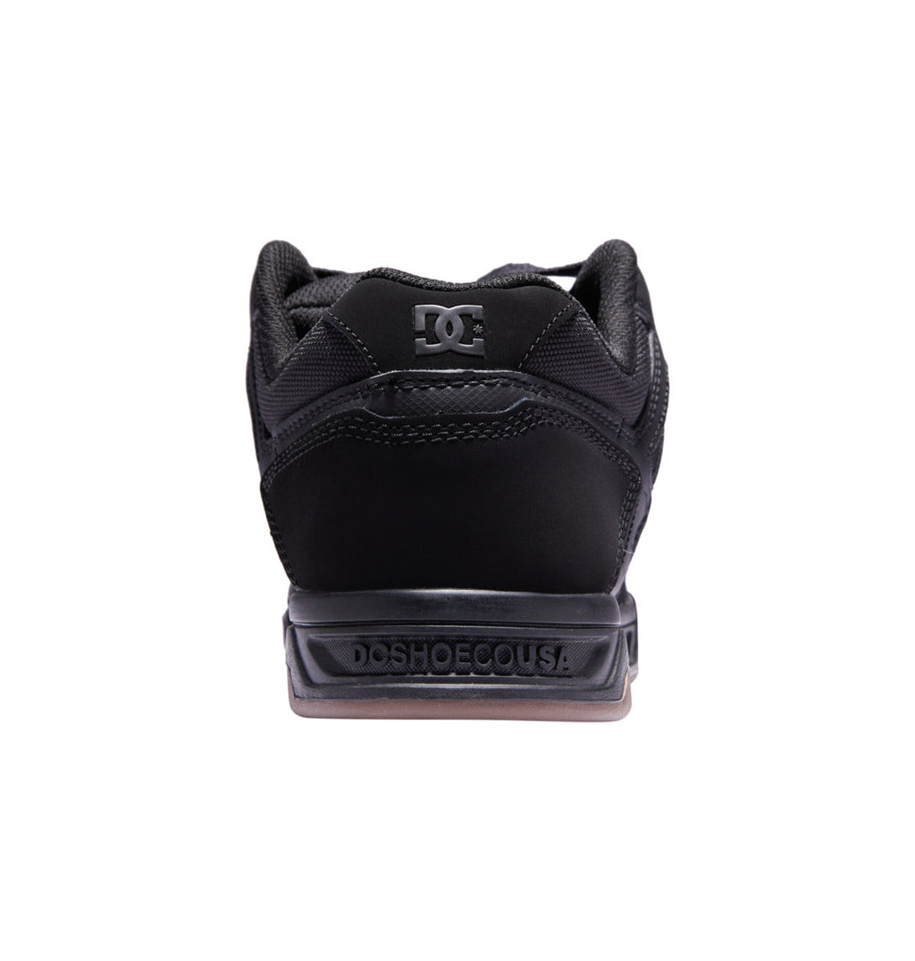 Back view of the DC Shoes Men’s Stag in black, with ‘DCSHOECOUSA’ embossed on the heel and the DC logo on the tongue, featuring an oversized puff and durable cupsole construction, shown against a white background.