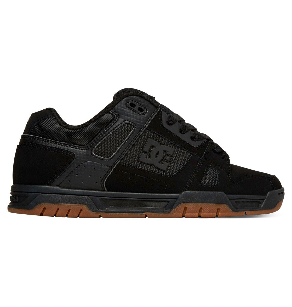 The DC Shoes Men’s Stag Shoes are shown in side view against a white background, featuring a black low-profile design with mesh and suede uppers, black laces, perforated panels, and a durable brown cupsole.