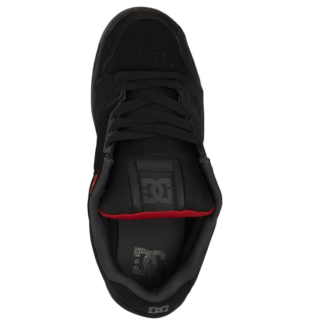 A top view of the Men’s Stag Shoes by DC Shoes reveals a black skate shoe with black laces, a red accent on the side, and prominent DC logos on the tongue and insole—showcasing its technical design and durable cupsole, signature features of DC Shoes.