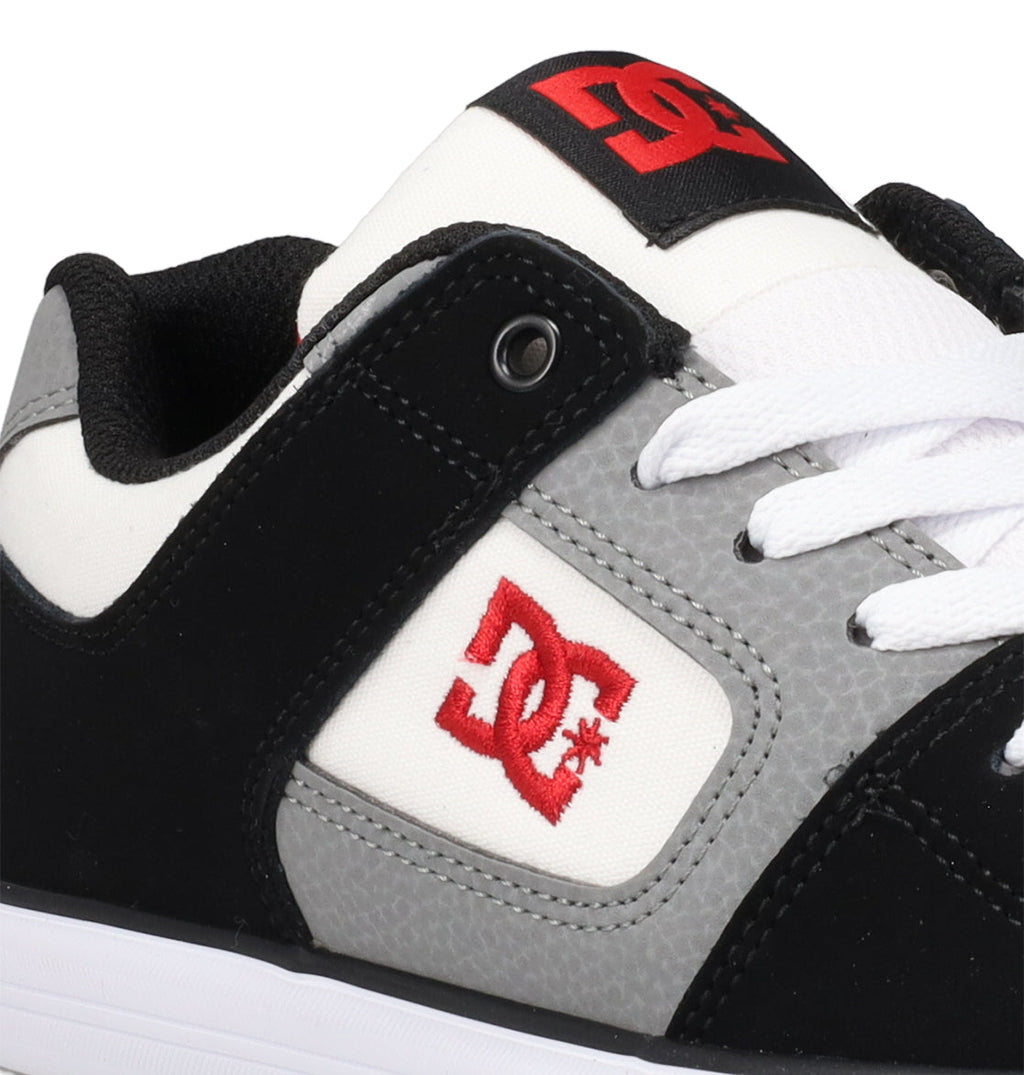 A close-up of the DC Shoes Kids’ Pure Shoes in black, gray, and white, featuring white laces and a red DC logo on the side and tongue, designed for durability and comfort in everyday wear.