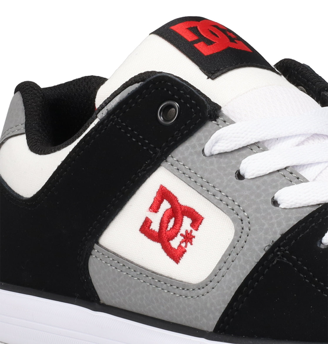 A close-up of the DC Shoes Kids’ Pure Shoes in black, gray, and white, featuring white laces and a red DC logo on the side and tongue, designed for durability and comfort in everyday wear.