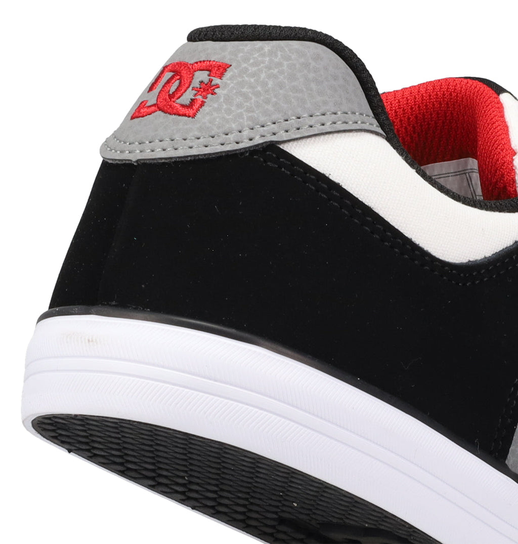 Close-up of the heel of the Kids’ Pure Shoes by DC Shoes, a black and white sneaker with gray and red accents. Features a red DC logo on the back and a durable white rubber sole—perfect for comfortable kids’ skate shoes.
