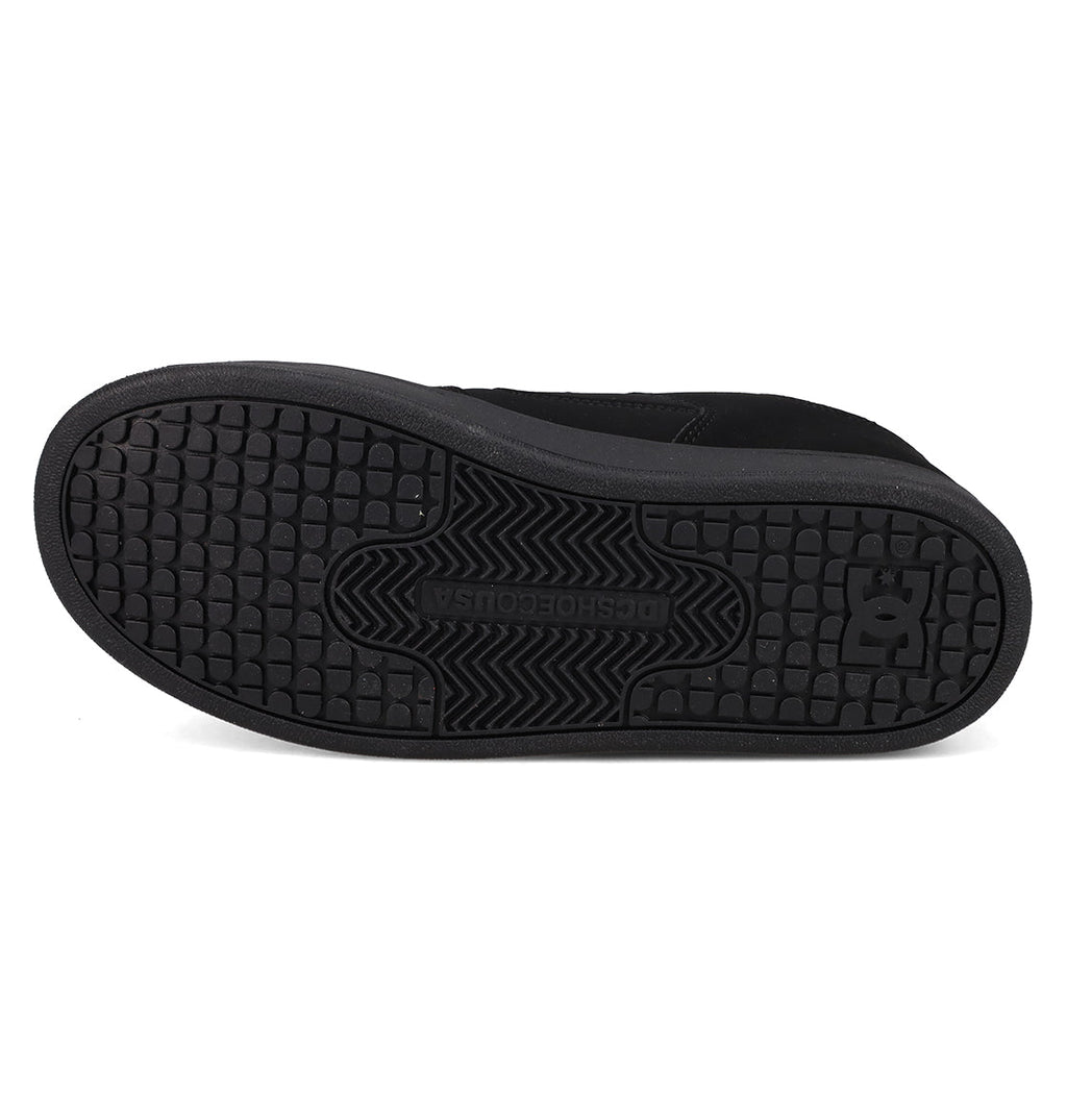 The image displays the black rubber sole of the DC Shoes Kids’ Manteca 4 V Shoes, viewed from the bottom, highlighting the tread pattern and prominent DC logo near the heel—a signature feature of these durable and kid-friendly sneakers from DC Shoes.