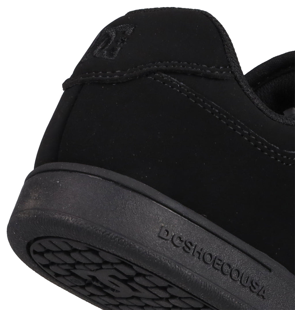 Close-up of the heel and sole of a black Kids’ Manteca 4 V Shoe from DC Shoes, with “DC SHOESCOUSA” embossed on the midsole. This sneaker, part of the Manteca skate shoes collection, showcases visible stitching, durable suede accents, and a textured rubber outsole.