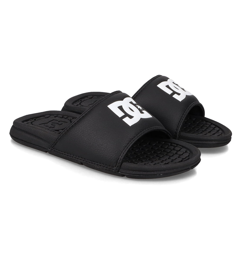 A pair of Kids' Bolsa Slides from DC Shoes in black with open toes and bold white DC logos on the straps, shown on a white background.