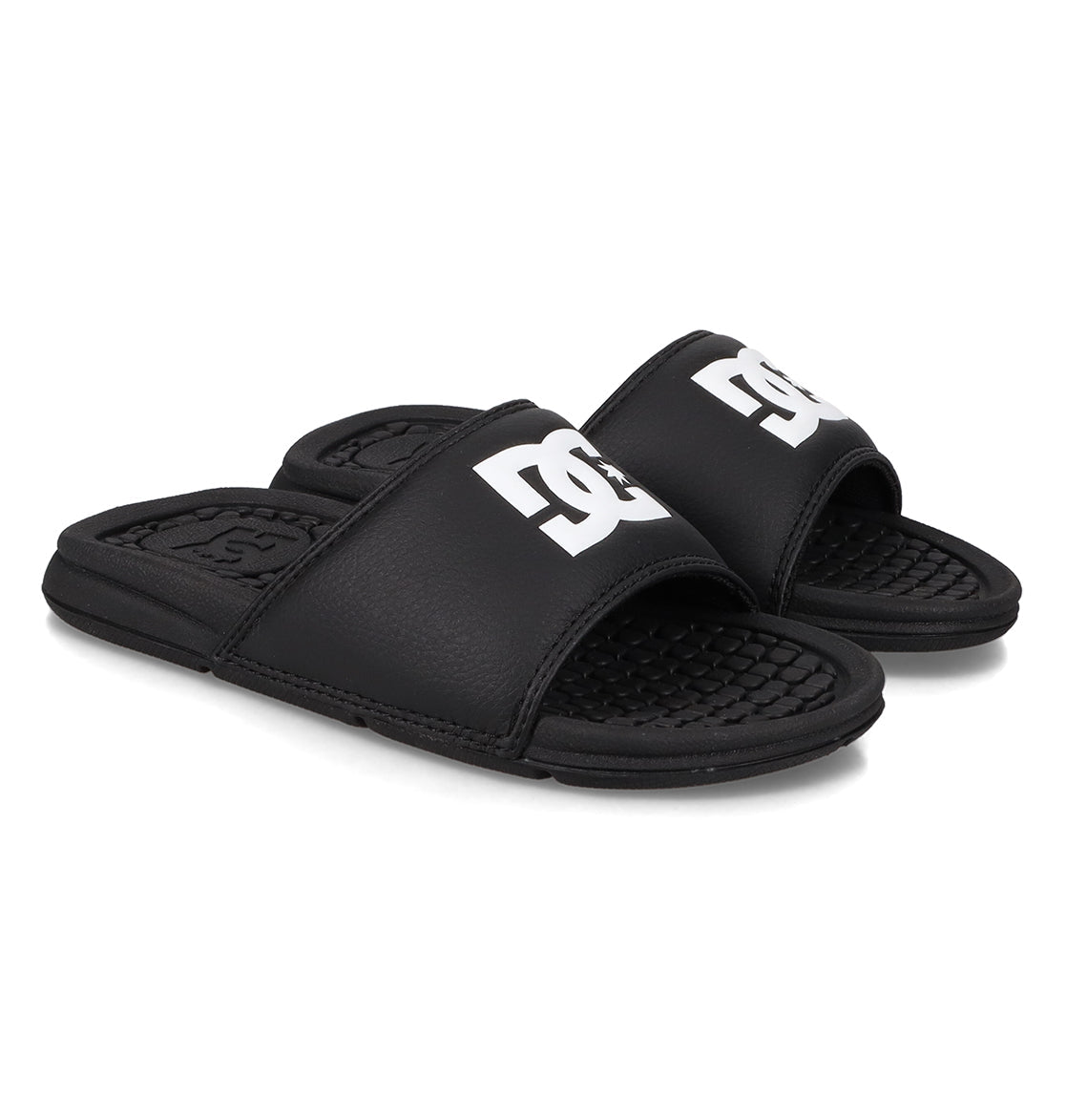 A pair of Kids' Bolsa Slides from DC Shoes in black with open toes and bold white DC logos on the straps, shown on a white background.