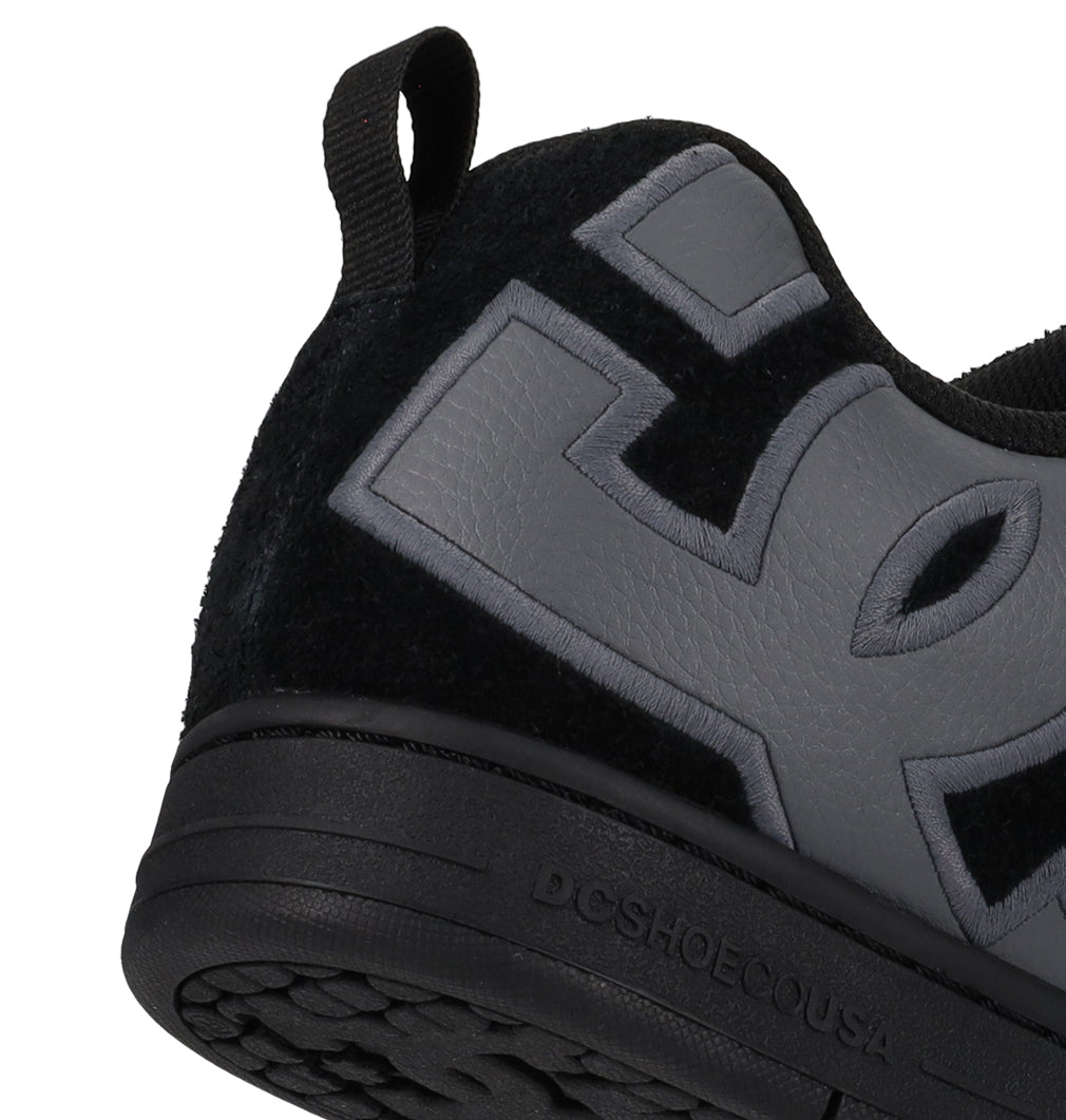 Close-up of the heel and side of the black DC Shoes Men’s Court Graffik Special Edition shoe with a puffy silhouette, featuring oversized gray branding and a back loop. The textured two-tone sole is embossed with “DGSHOEOUSA.”.
