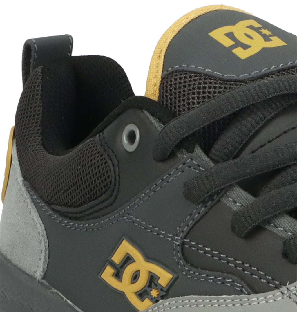Close-up of a dark gray and yellow Men’s Ascend Skate Shoe by DC Shoes, inspired by the legendary Josh Kalis and embodying signature DC design elements, featuring the DC logo on the side and tongue, with black laces and mesh material near the ankle.