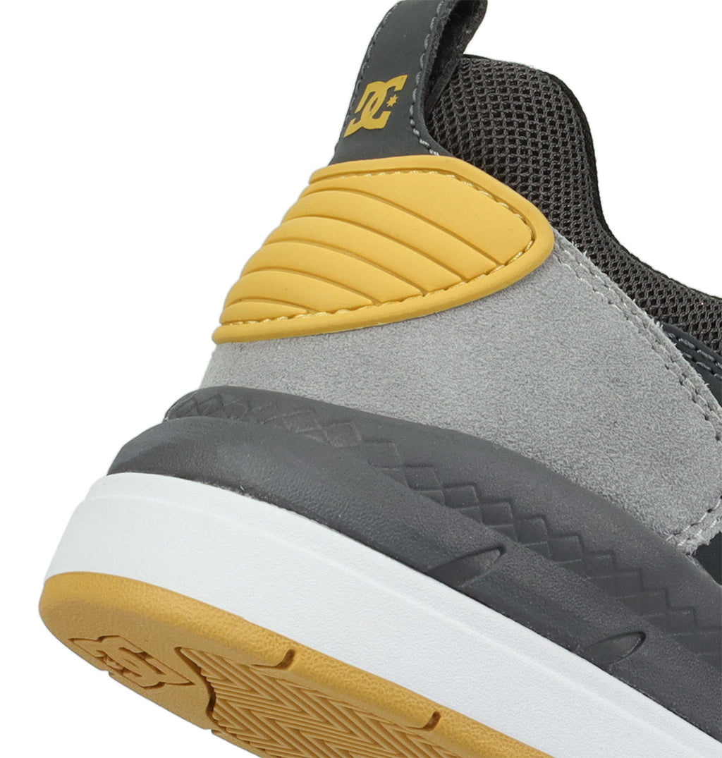 Close-up of the heel of the Men’s Ascend Skate Shoes by DC Shoes, highlighting gray, yellow, and white accents. The iconic DC logo appears near the ankle, emphasizing classic brand style. This sneaker combines suede, mesh, and rubber materials for contemporary comfort.