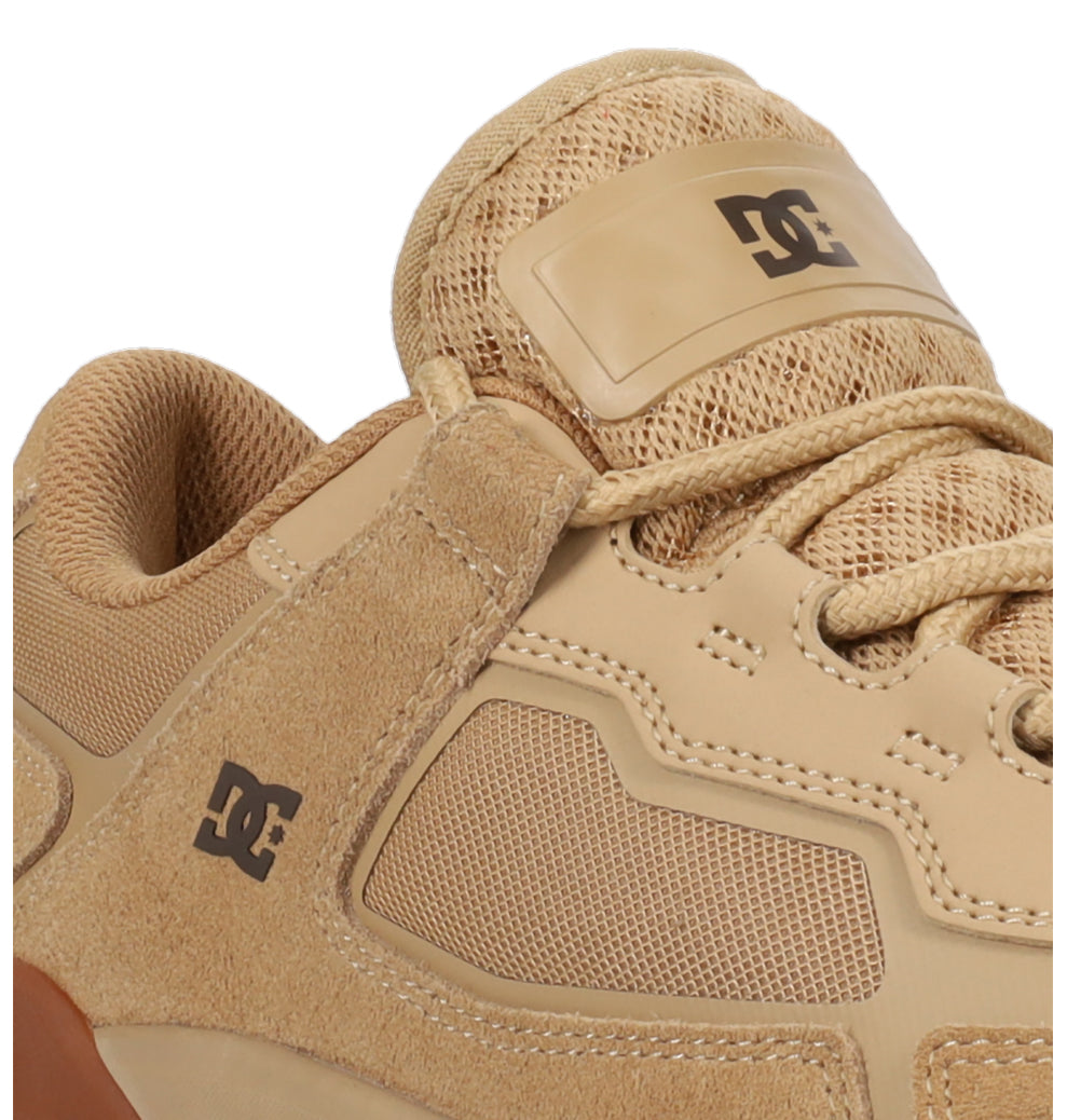 Close-up of a tan Men’s Metric Skate Shoe by DC Shoes, featuring the DC logo on the side and tongue, a mix of suede, mesh, and leather textures, beige laces, detailed stitching, and a durable outsole designed for enhanced impact protection.