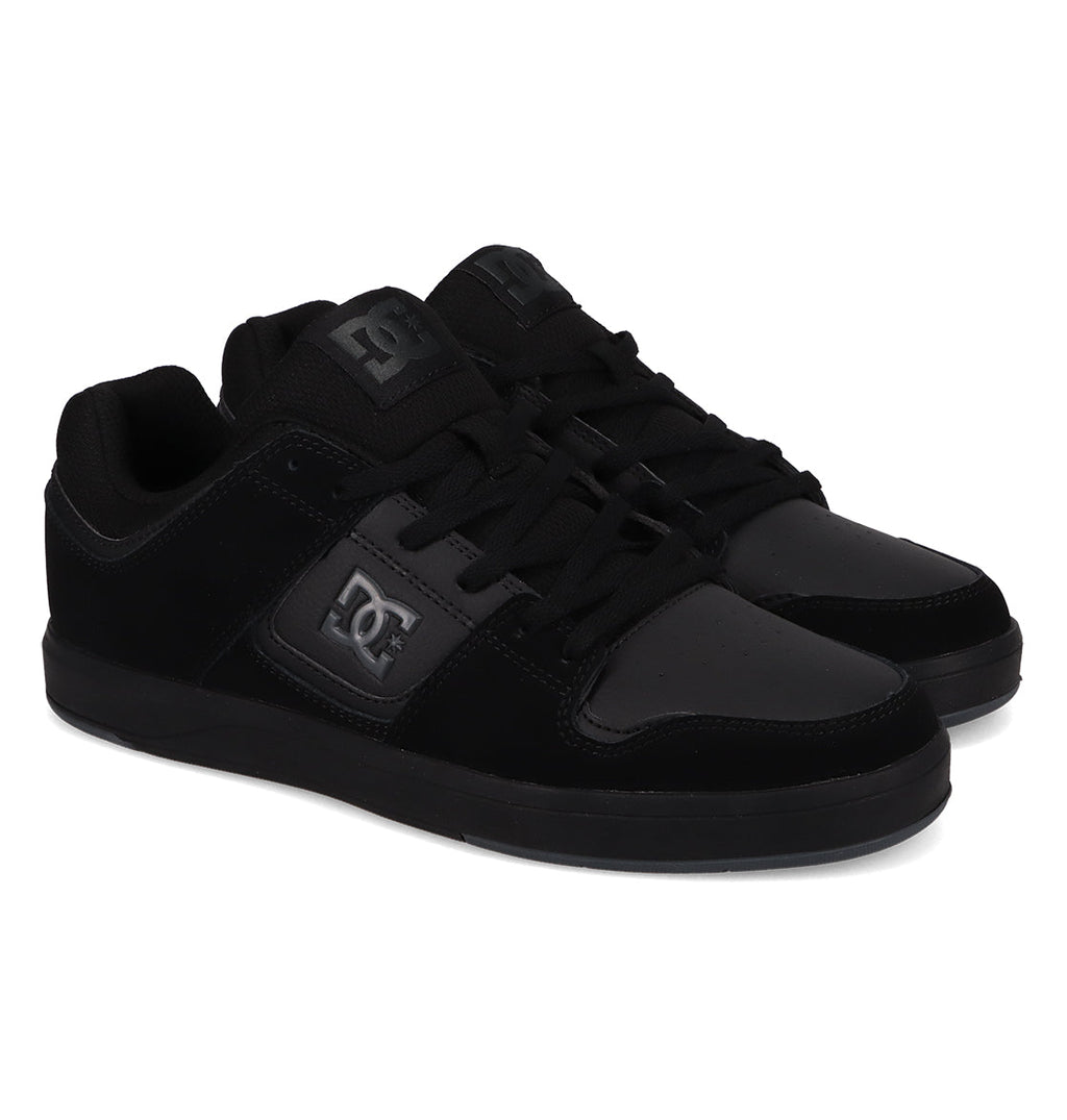A pair of Men’s DC Cure Shoes from DC Shoes, featuring a durable black leather suede upper, lace-up fronts, black soles, and the signature DC logo on the side. The shoes are positioned slightly angled, side by side, against a white background.