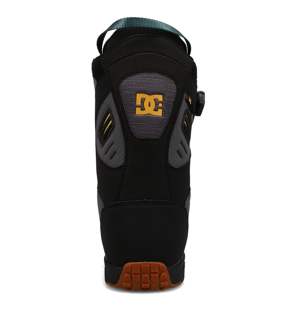 Back view of the DC Shoes Men’s Judge Snowboard Boots in black, featuring a gray and yellow DC logo, a teal pull loop, and a brown treaded sole—an ideal choice for men’s snowboard footwear.