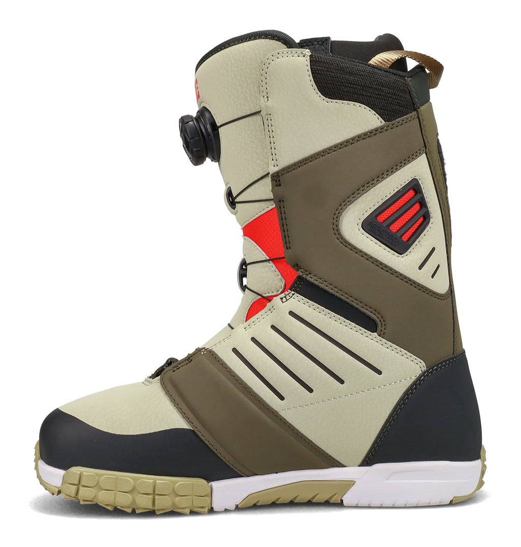The DC Shoes Men’s Judge Snowboard Boots are shown in a left side profile against a white background, featuring a tan upper with black and olive accents, red detailing, a durable rubber sole, and a dial lacing system on the side.