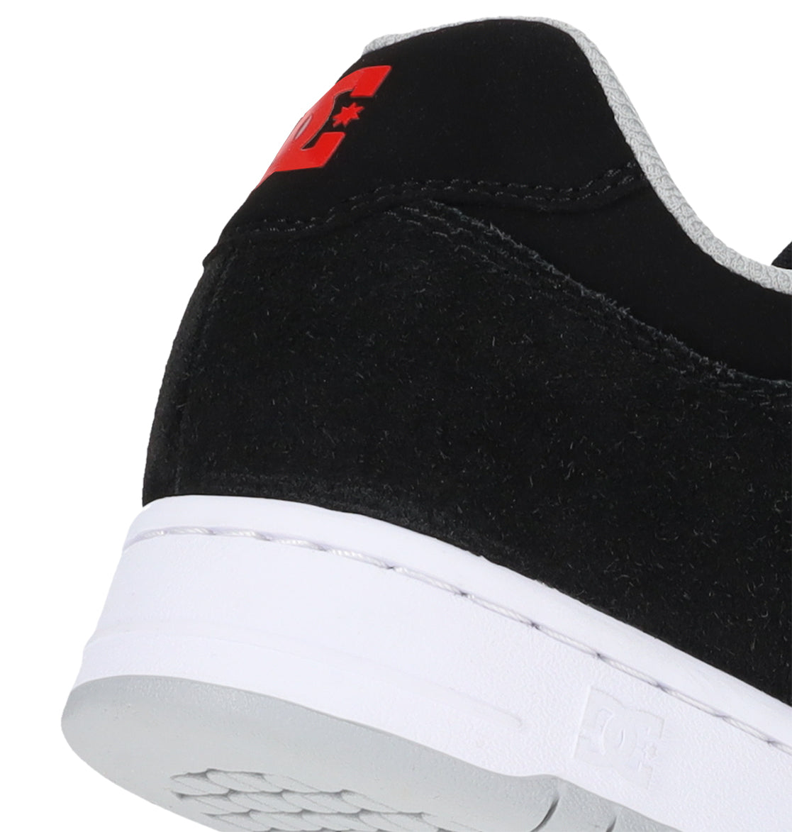 Close-up of the heel of the Men’s Manteca 4 Shoes by DC Shoes, featuring a black suede upper with a white sole and red DC logo on the back—showcasing detailed texture and part of the outsole, while highlighting modern comfort and premium performance skate shoe design.