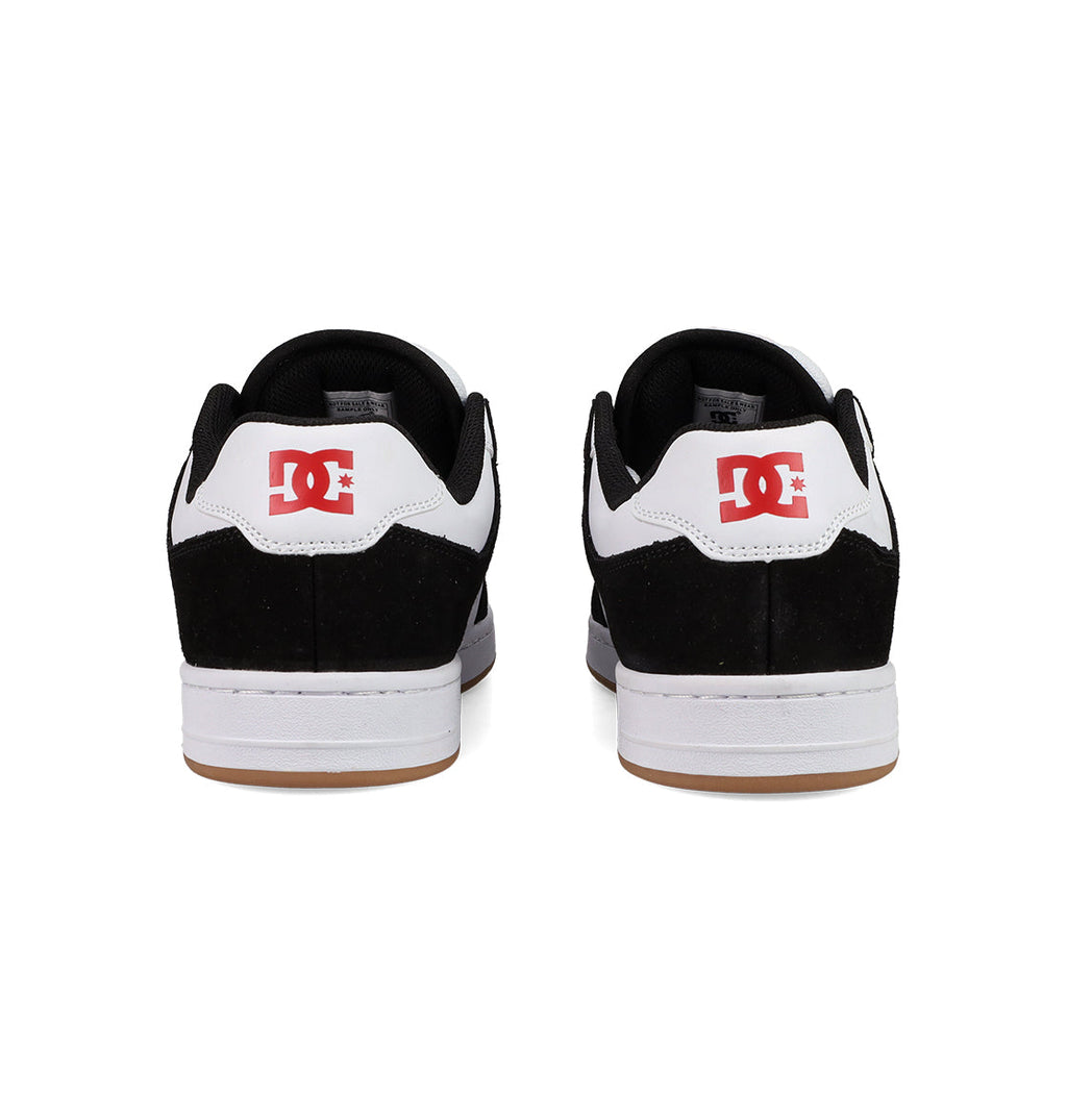The Men's Manteca 4 Shoes by DC Shoes feature a classic black and white design, visible red DC Shoes logos on the heels, white midsoles, and gum-colored outsoles, shown here from the back.