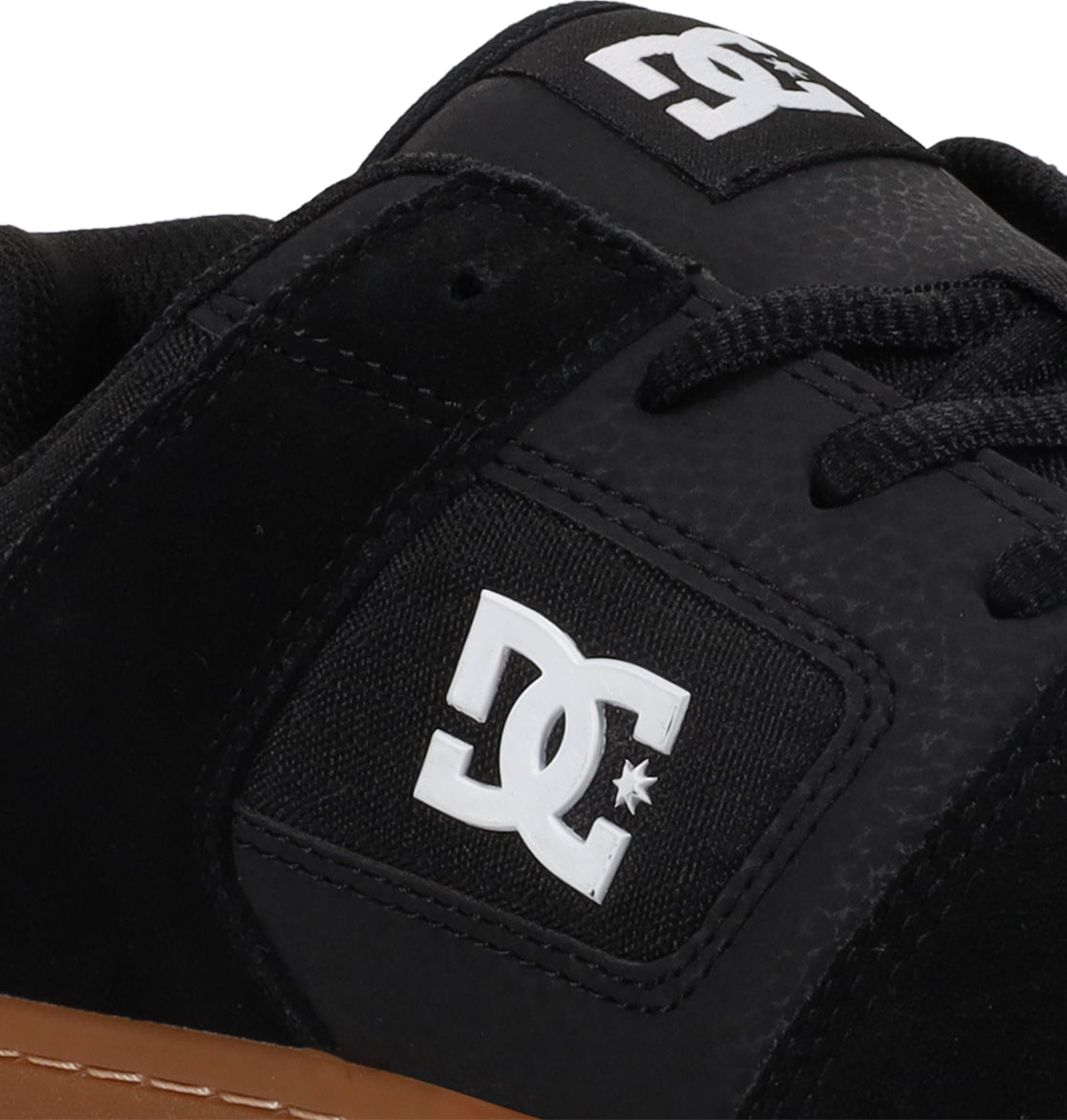 Close-up of the Men’s Manteca 4 Shoes by DC Shoes in black, featuring a white DC Shoes logo on the side and tongue. These shoes have black laces, a brown gum rubber sole, and deliver modern comfort ideal for both everyday wear and skate sessions.