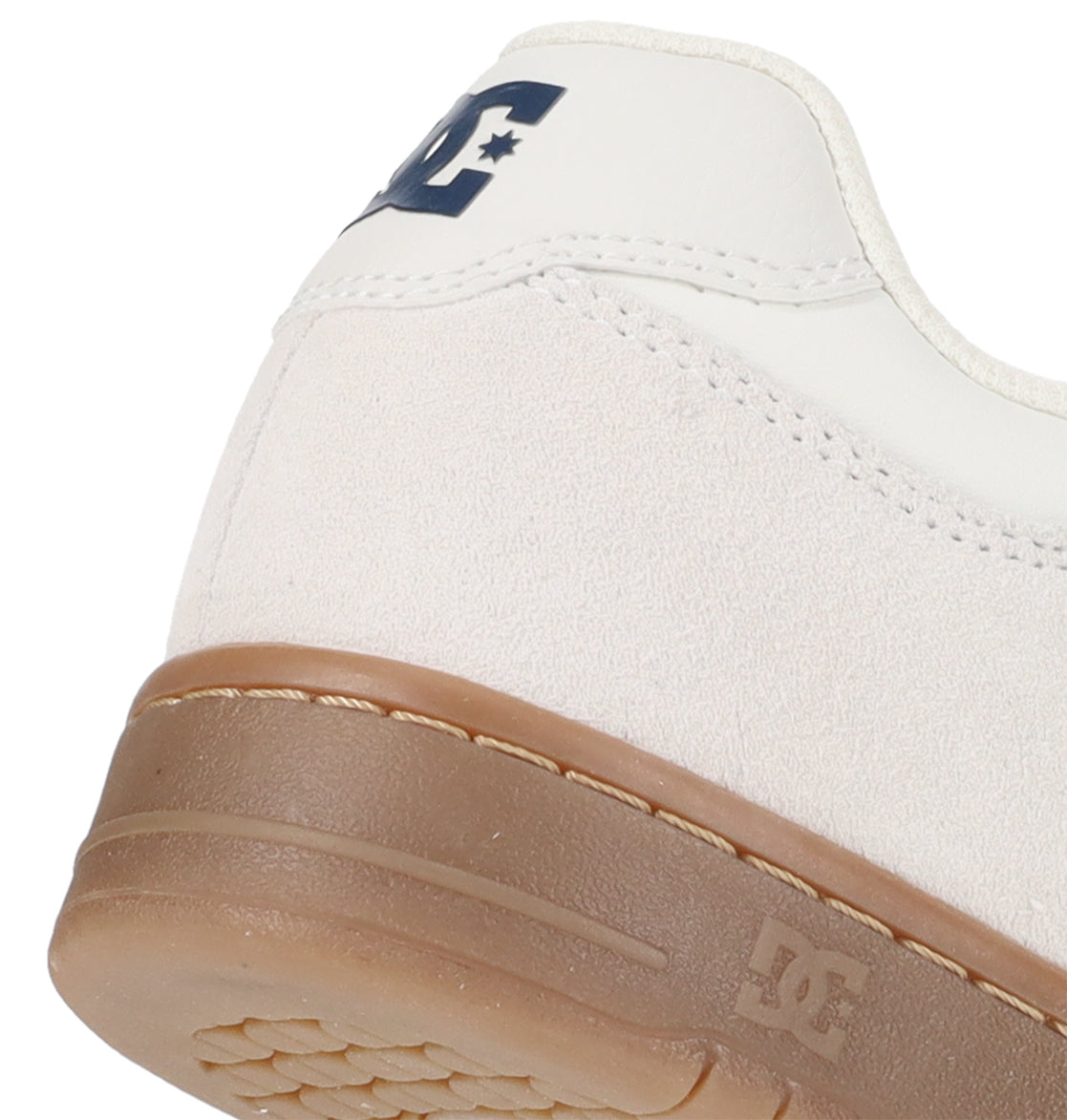 Close-up of the heel of a white DC Shoes Men’s Manteca 4 sneaker with a brown rubber sole, highlighting its performance-focused design. The navy DC Shoes logo is visible on the back and side, while the upper features a blend of leather and suede in the classic Manteca style.