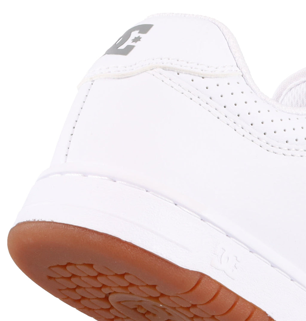 Close-up of the heel of a white Women's Manteca 4 Shoe by DC Shoes, featuring a brown rubber sole, gray DC Shoes logo on the back, and perforated detailing near the collar for a performance-focused look.