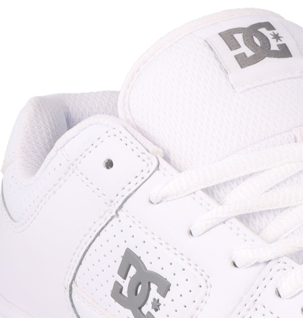 Close-up of a white DC Shoes Women’s Manteca 4, featuring the gray DC logo on both the side and tongue, complemented by white laces and textured fabric. Designed for style and comfort, these skate shoes showcase the brand’s performance-focused craftsmanship.