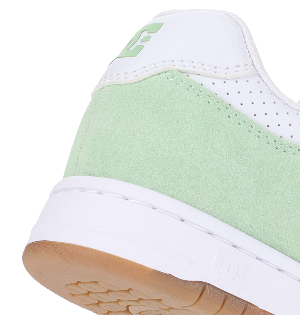 Close-up of the heel of the DC Shoes Women’s Manteca 4 sneaker in green and white, featuring a suede texture, a white sole with a light brown outsole, and part of the signature logo on the back—highlighting the performance-driven design inspired by DC Shoes’ classic Women’s Manteca collection.