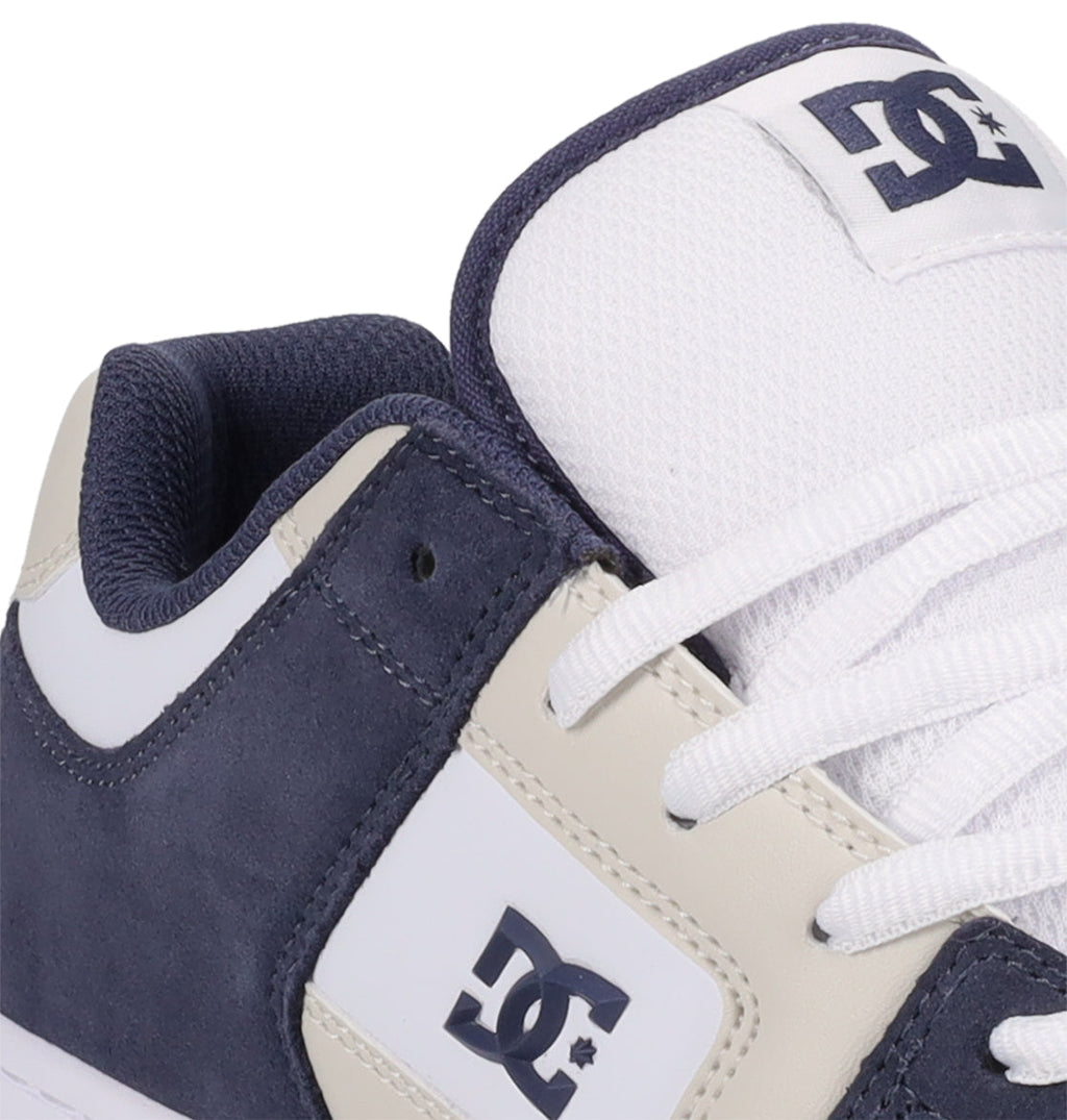 Close-up of a navy blue and white Men’s Manteca 4 Shoe by DC Shoes, featuring the signature side logo, crisp white laces, a padded collar, and a breathable mesh tongue adorned with the DC Shoes emblem—a prime showcase of the brand’s performance-driven design.