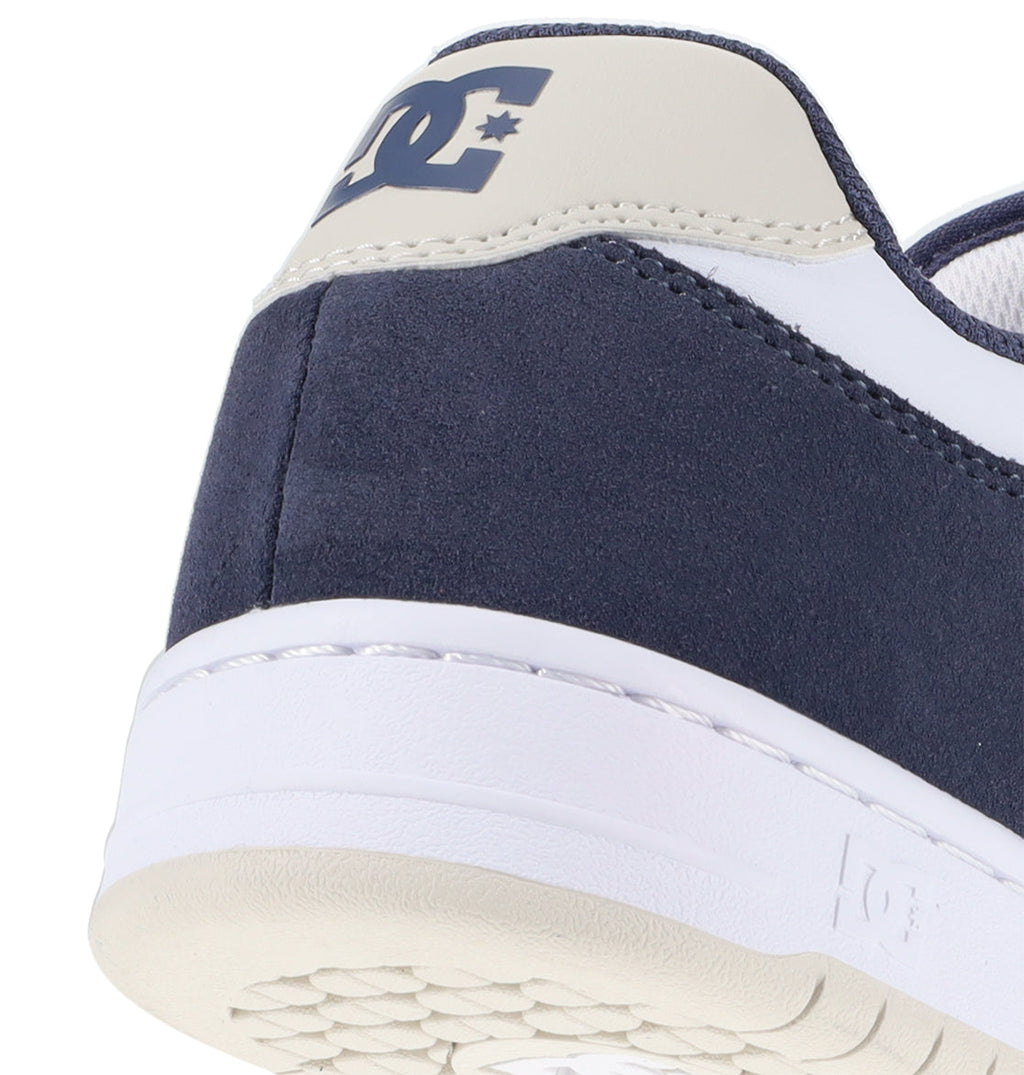 Close-up of the heel of a navy blue and white Men’s Manteca 4 Shoe by DC Shoes, featuring the DC Shoes logo on the back and a glimpse of the white sole with its textured underside—a clear reflection of its performance-driven design.