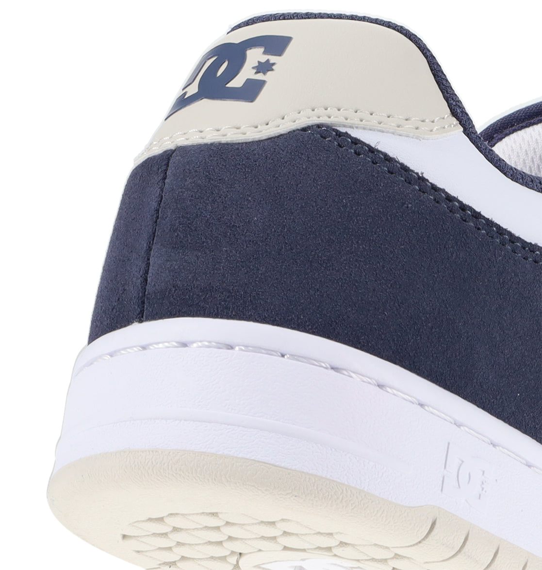 Close-up of the heel of a navy blue and white Men’s Manteca 4 Shoe by DC Shoes, featuring the DC Shoes logo on the back and a glimpse of the white sole with its textured underside—a clear reflection of its performance-driven design.