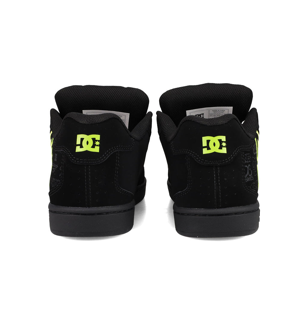 A pair of Men's Net Shoes by DC Shoes in black, seen from the back with neon yellow DC branding on the heels, padded black collars, and a durable, puffy skate sneaker design.