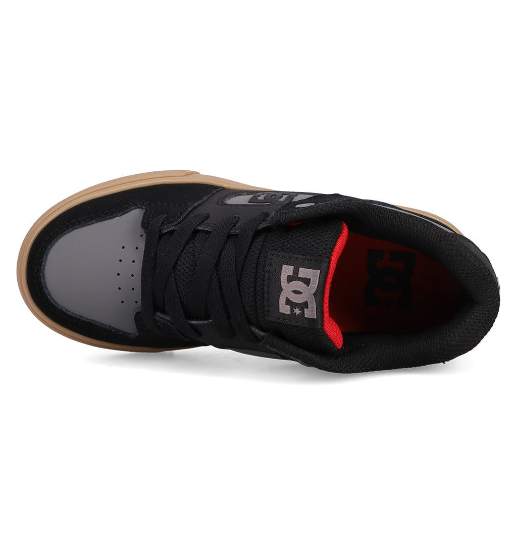 Top view of Kids' Pure Shoes by DC Shoes in black and gray with black laces, gum sole, and red heel lining. The tongue displays a white DC logo. These versatile shoes offer style and comfort for any occasion.