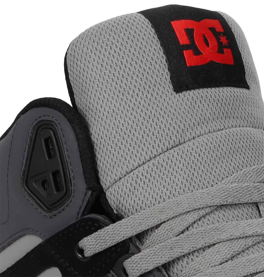 Close-up of the Men’s Pure High Shoes by DC Shoes, featuring a gray upper with a mesh tongue, gray laces, and a black patch adorned with the signature red DC Shoes logo—ideal for anyone seeking comfortable footwear that combines style and everyday versatility.