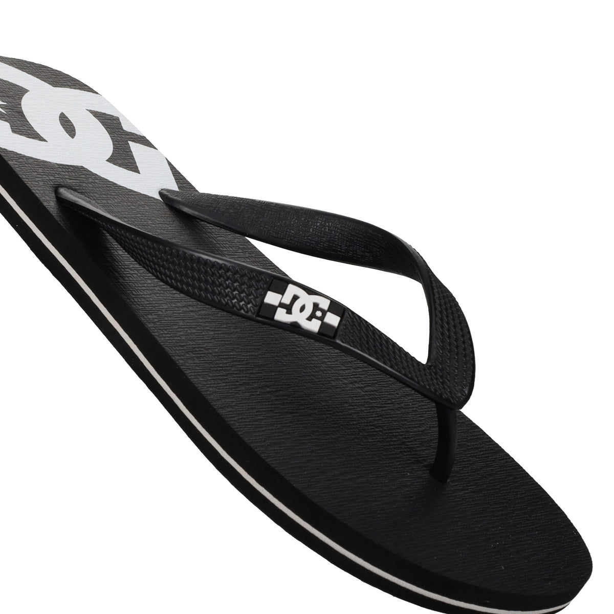 A close-up of the Men’s Spray Slides by DC Shoes showcases a black flip-flop sandal with a white DC logo on the strap and footbed, featuring a textured surface and white accents—these must-have slides are perfect for relaxing after a skate session.