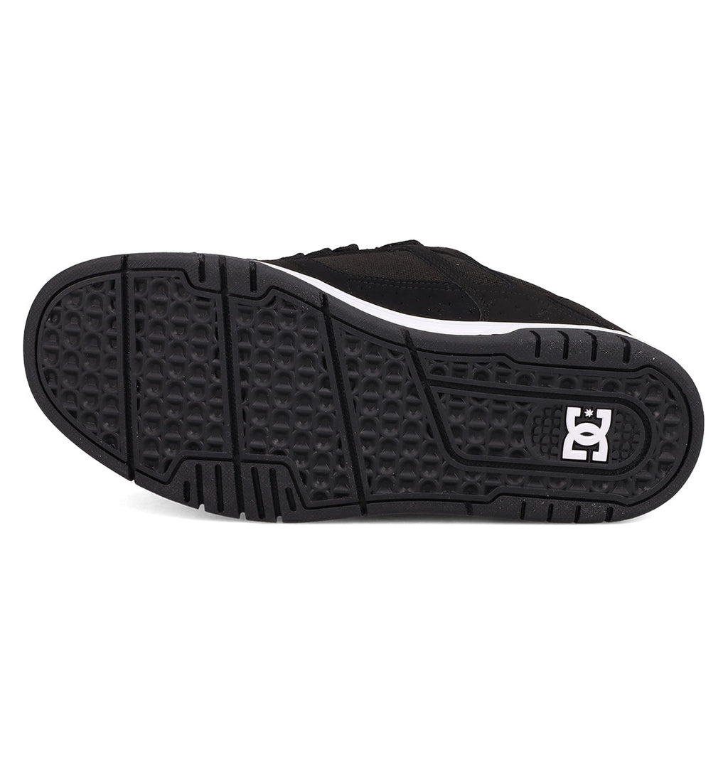 The image features the black rubber sole of DC Shoes Men's Stag Shoes, displaying a textured grip and the white DC logo near the heel. Part of the black upper is visible, highlighting classic skate style and cupsole construction.