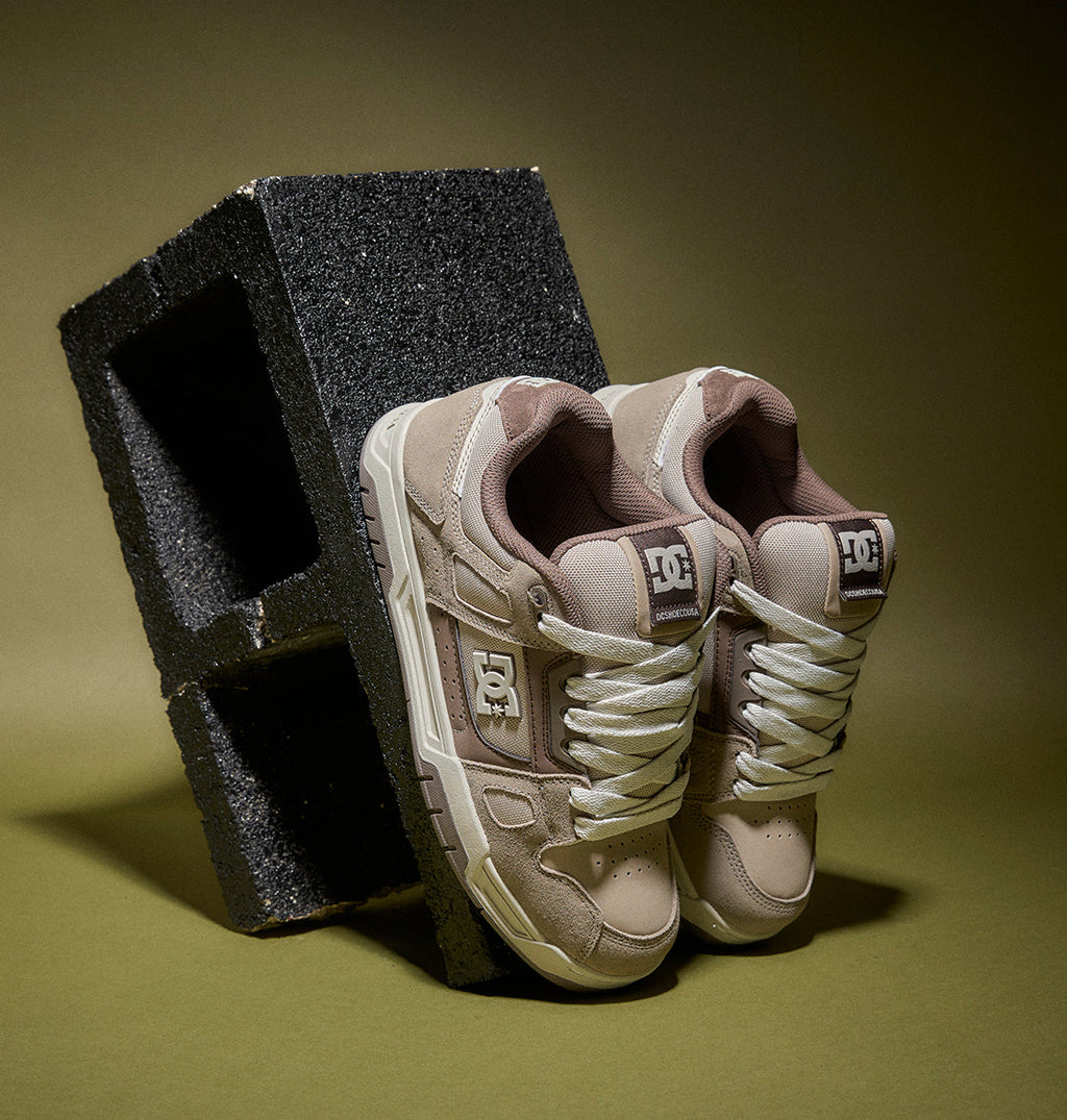 Pair of beige sneakers with white soles on a green background
