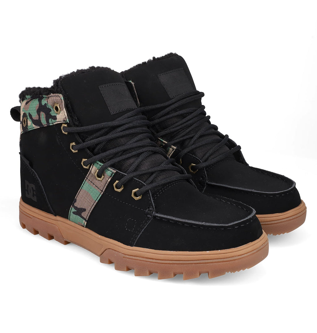 The DC Shoes Men's Woodland Winter Boots feature black uppers, tan rubber soles, black laces, green camo ankle accents, metal eyelets, and a rugged design—ideal for outdoor winter wear.