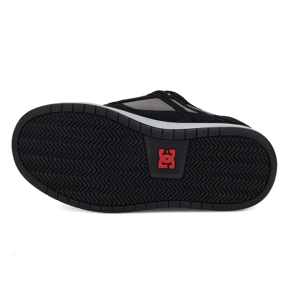 Bottom view of the DC Shoes Kids’ Stag Shoe in black, showcasing a herringbone tread pattern and a red DC Shoes logo near the center of the durable rubber sole, designed for enhanced impact absorption and lightweight cushioning.
