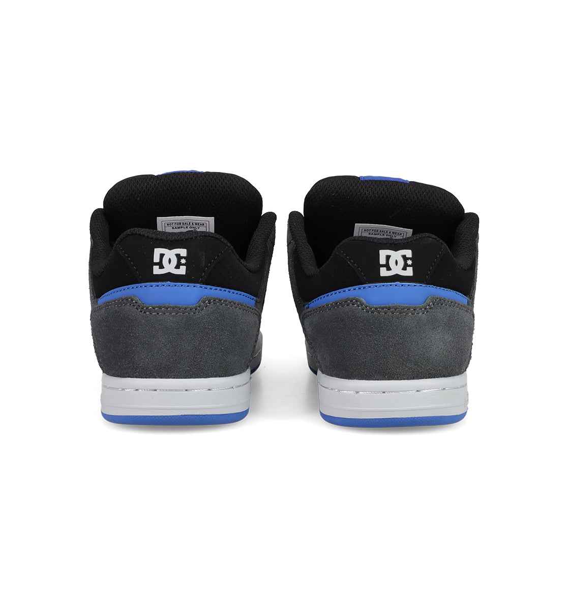 A pair of Kids' Stag Shoes by DC Shoes seen from the back, featuring black and grey suede uppers, blue trim, white soles, cupsole construction, and the DC logo on the heel.