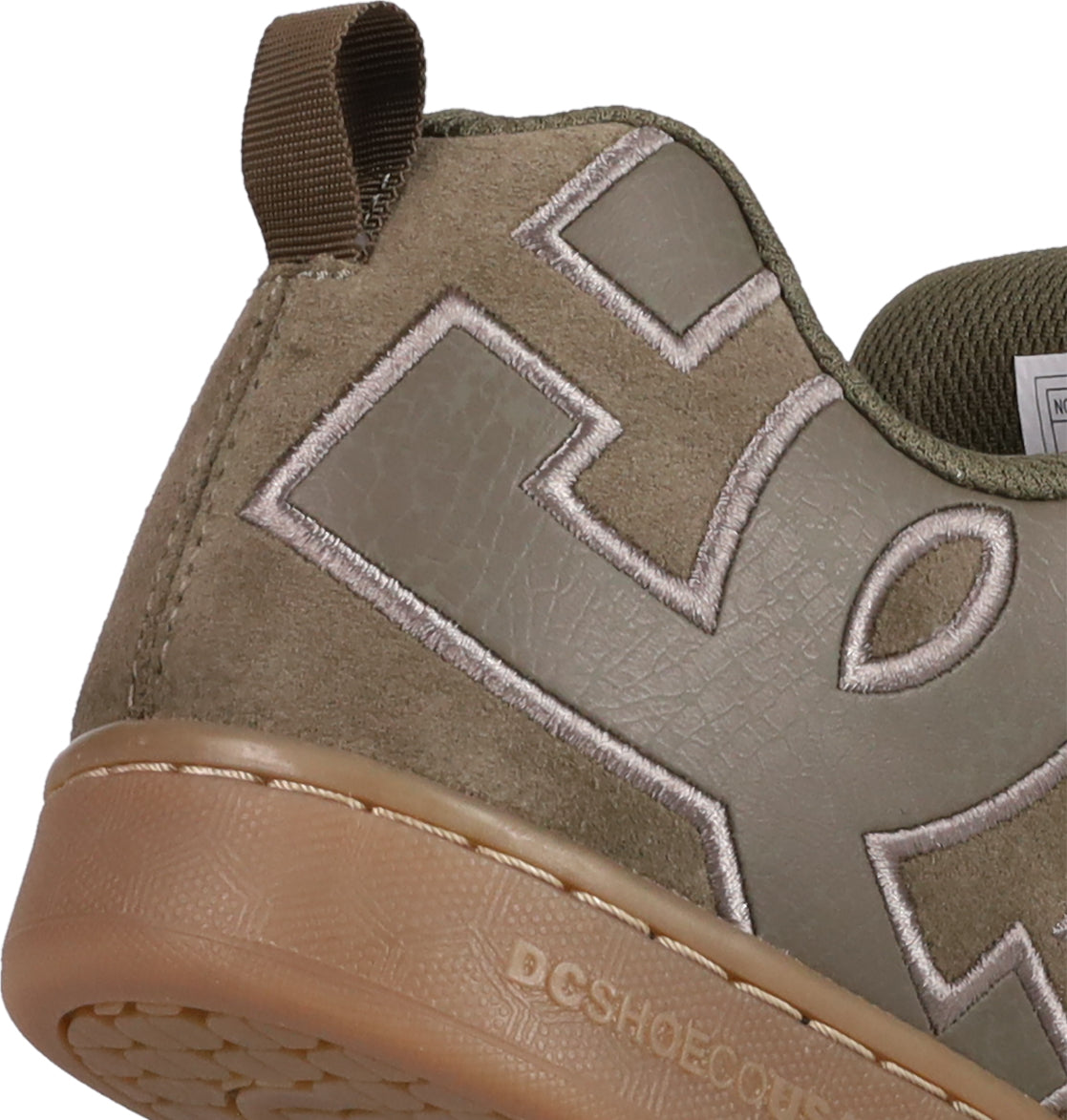 Close-up of the heel of DC Shoes Women's Court Graffik SD sneaker, featuring tan and brown suede upper, large stitched letters, a textured rubber sole, brown pull tab at the back, trendy colorways, and visible stitching.
