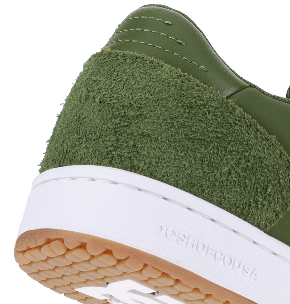 Close-up of the heel of the DC Shoes Men’s Astrix skate shoe, featuring a green textured suede panel, a white midsole, and a gum rubber outsole designed for superior board control in street skateboarding. The word DCSHOECOUSA is embossed on the sole.