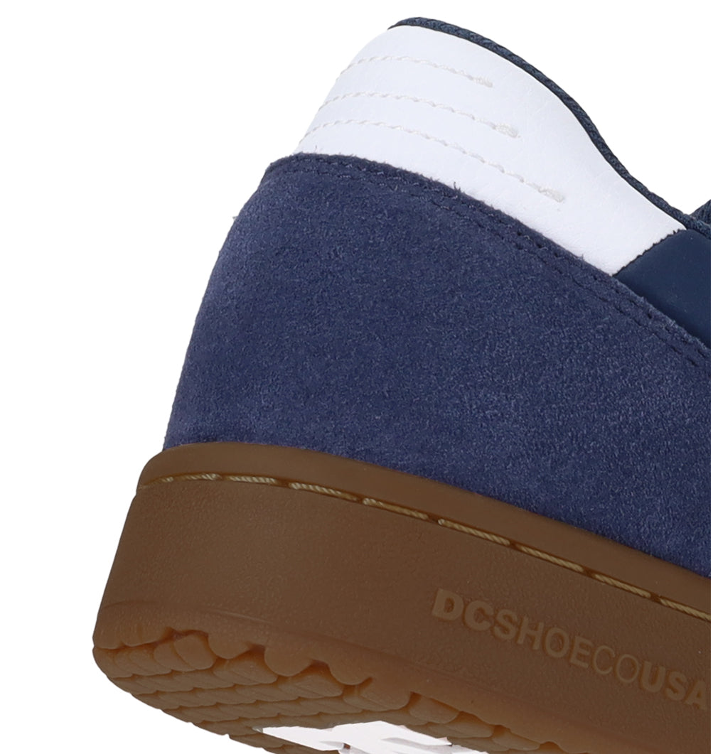 Close-up of the heel of the Men’s Astrix Shoes by DC Shoes, featuring a blue suede upper, white accent, and a brown rubber sole engineered for exceptional board control. The DC Shoes logo is embossed on the side of the sole, making these shoes perfect for street skateboarding.