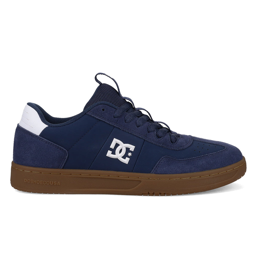 A left-side profile of the Men’s Astrix Shoes by DC Shoes is displayed against a white background. This navy blue and white skate shoe is designed for street skateboarding, featuring suede accents for enhanced board control, a brown sole, and a white DC Shoes logo on the side.