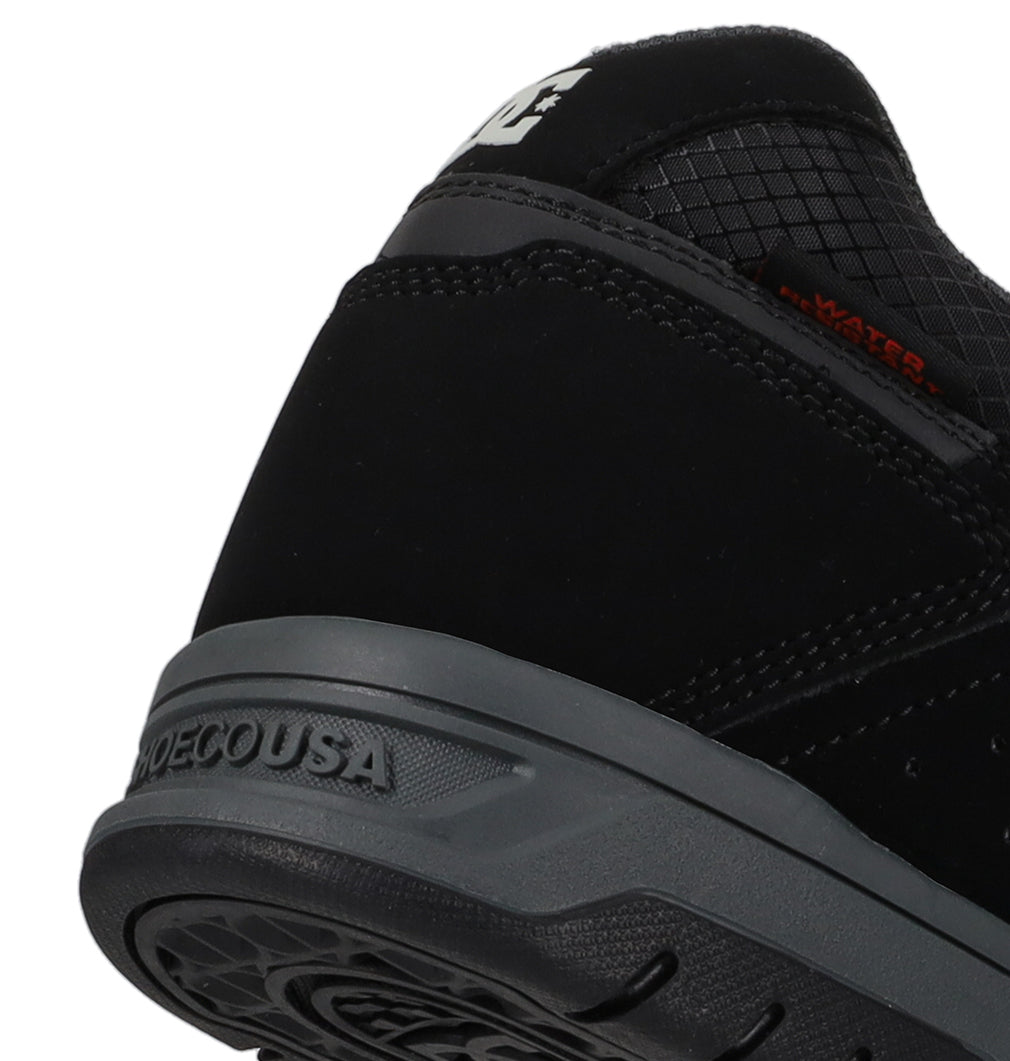 Close-up of the heel of a black DC Shoes Men’s Stag Winterized Shoe featuring a grey sole. “DCSHOECOUSA” is embossed on the sole, while “WATER” appears in orange text on the upper portion. The shoe showcases a subtle stitched design and provides lightweight cushioning for enhanced comfort with every step.