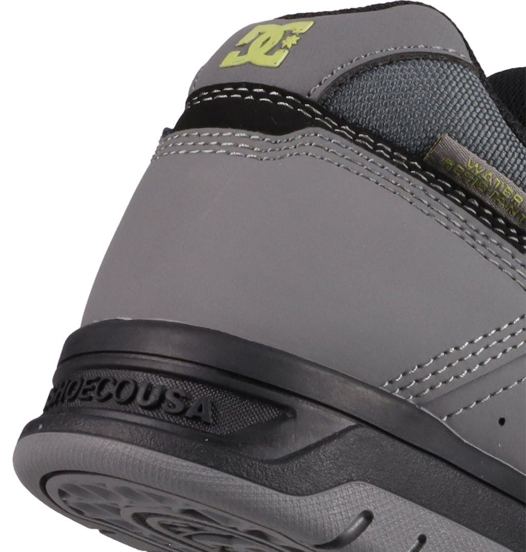 Close-up of the heel of DC Shoes Men's Stag, a gray sneaker with black and light green accents, visible stitching, durable cupsole, logo detailing, and a WATER RESISTANT tag—merging style and skate heritage.