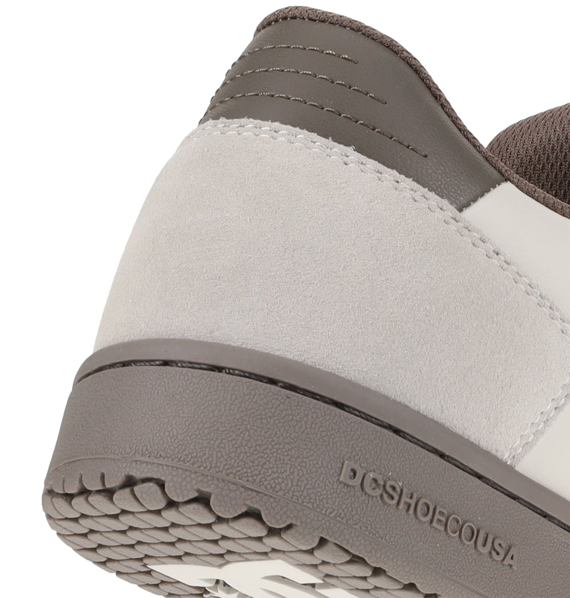 Close-up of the heel of the DC Shoes Men’s Astrix Shoe, featuring a gray sole, light gray suede upper, and dark gray leather accents. The DCSHOECOUSA logo is embossed on the outer sole edge, combining style and durability for superior board control during street skateboarding sessions.