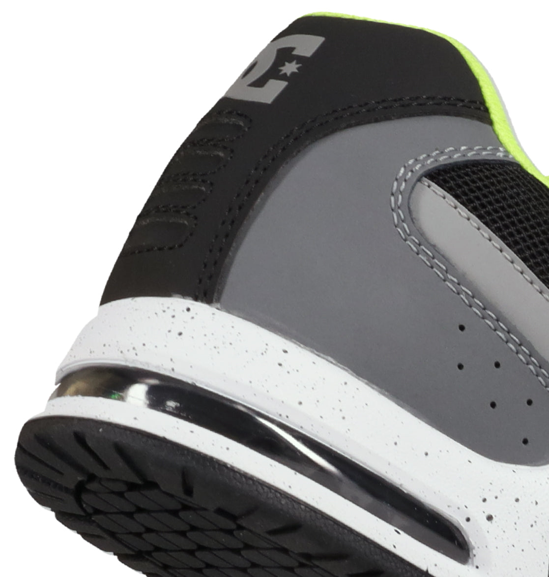Close-up of the heel and side of the DC Shoes Men’s AT-2 Shoes in gray and black, featuring a white speckled midsole, visible tread pattern, and neon yellow lining. A supportive TPU cage enhances stability around the heel, while part of the DC “E” logo appears on the back.