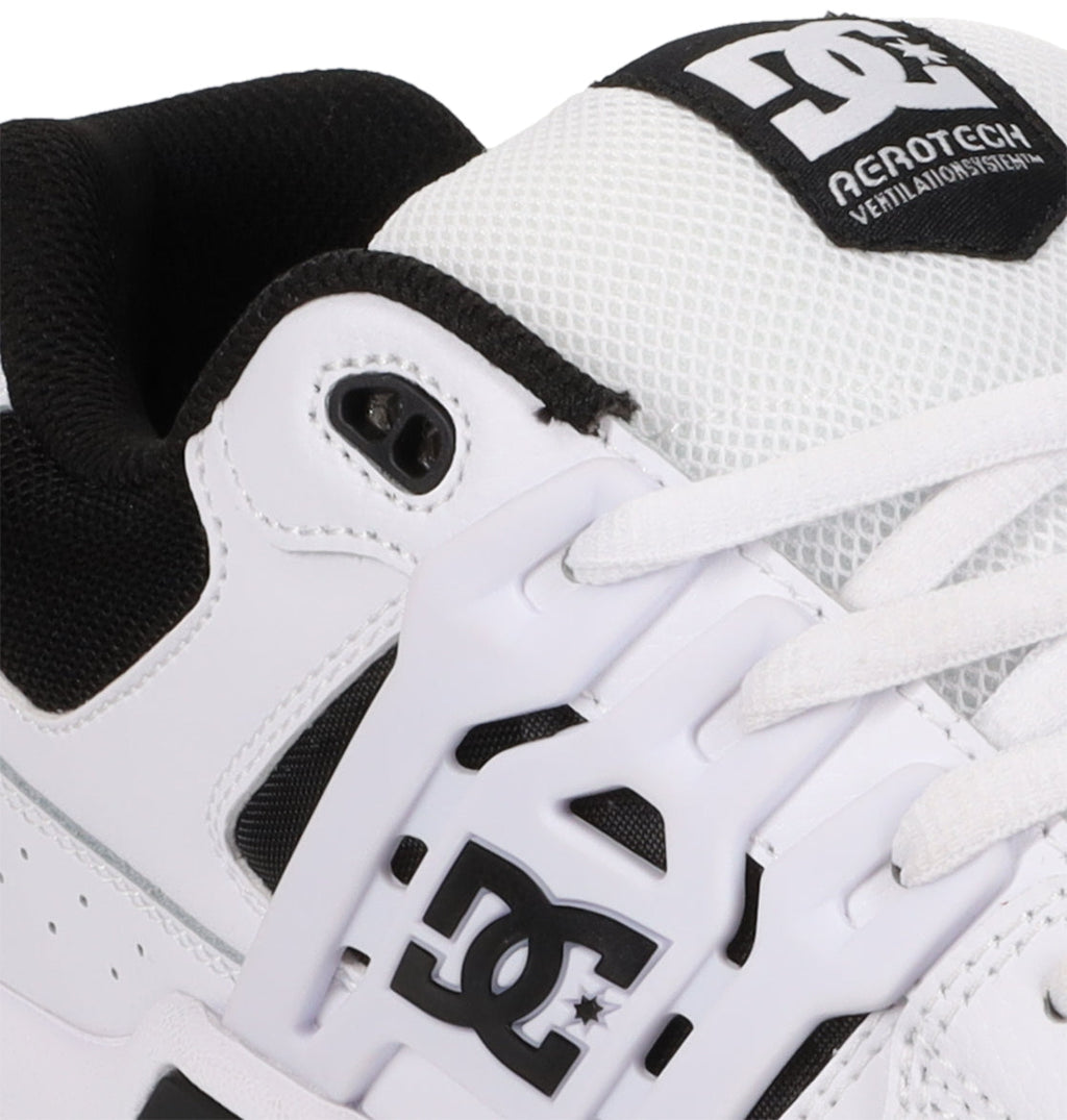Close-up of the Men’s AT-2 Shoes by DC Shoes in white and black, showcasing the DC Shoes logo and AEROTECH ventilation system text on the tongue, and featuring a supportive TPU cage for enhanced stability.